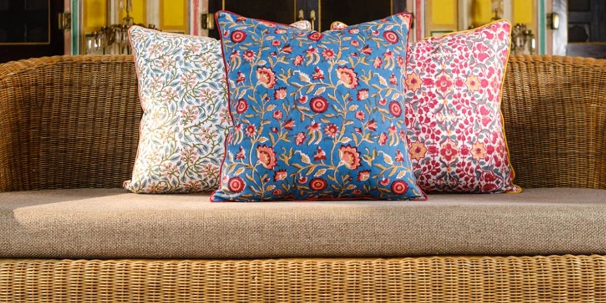 Three colorful floral-patterned pillows on a wicker sofa.