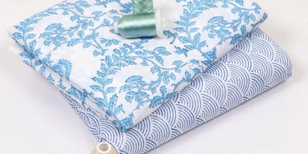 Two folded fabrics with blue patterns and thread spools.