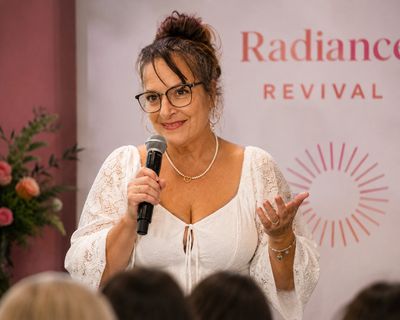 Woman in white dress speaking into a microphone at an event.