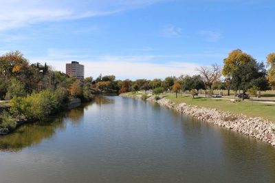 River flowing through a park with trees and a building.