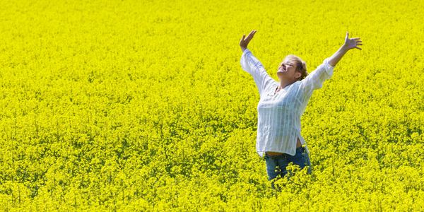 MOVING FRAGRANCE FORWARD woman in yellow field wth hands held high