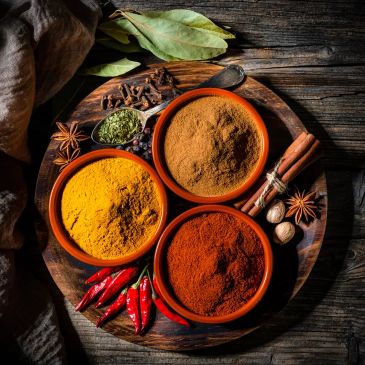 Three bowls of spices with herbs and chili on wooden tray.