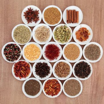 Various spices in white bowls arranged on a wooden surface.