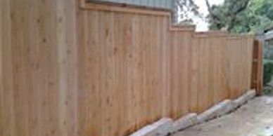 This privacy fence Austin with a cap and trim stair steps down a limestone retaining wall perfectly