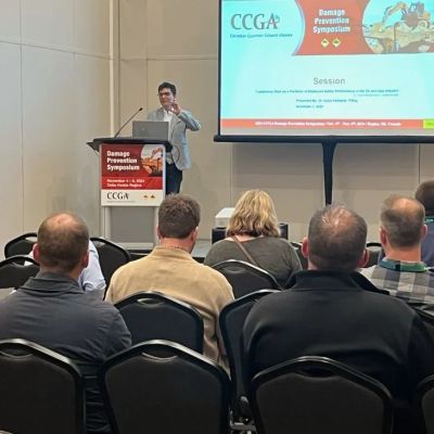 Speaker presenting at the Damage Prevention Symposium with audience seated.
