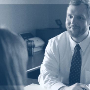 A man in a tie smiling during a conversation with a woman.