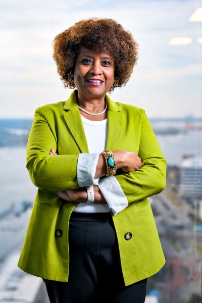 Confident woman in a green blazer smiling with arms crossed.