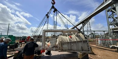 Heavy industrial equipment being lifted by crane outdoors.
