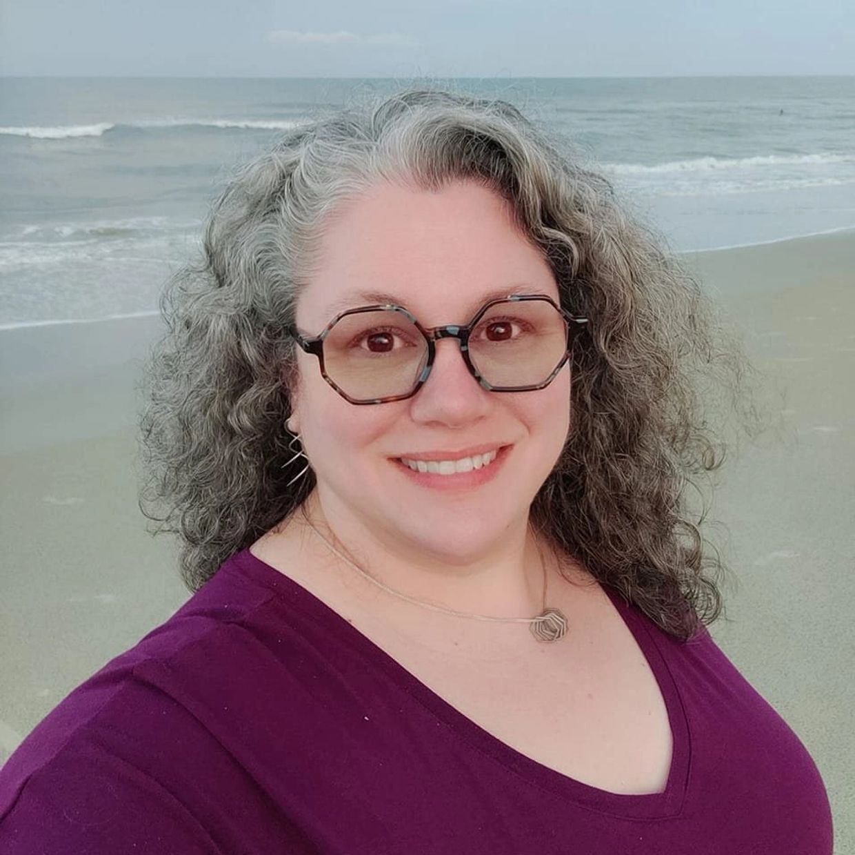 Woman smiling at the beach with glasses and curly hair.