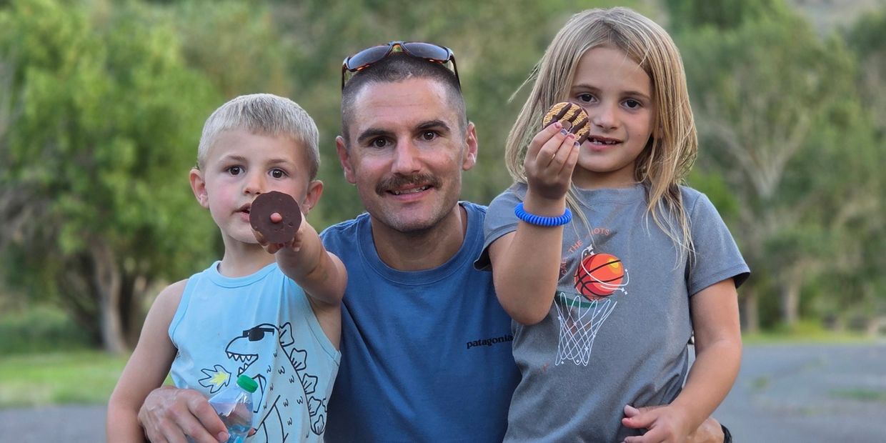 A father with his two children holding cookies and smiling outdoors.
