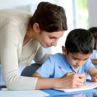 Teacher helping a young boy with his writing in class.