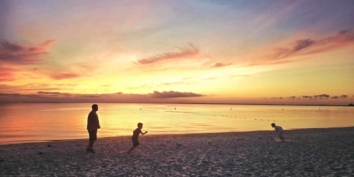 Silhouettes playing soccer on the beach at sunset.