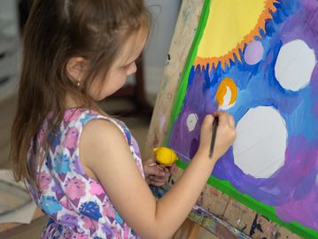 A young girl painting a colorful picture on an easel.