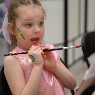 A young girl with face paint holding a paintbrush.