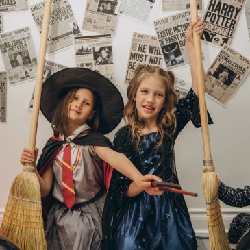 Two girls in Harry Potter costumes holding brooms and wand.