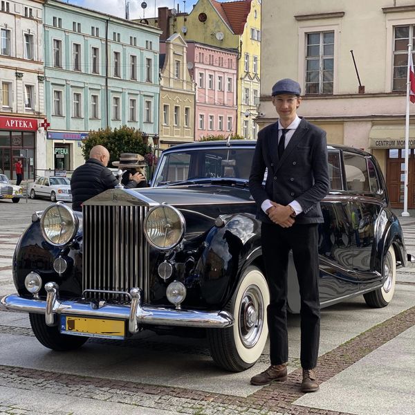Mężczyzna w garniturze stoi przy klasycznym Rolls-Royce w mieście.