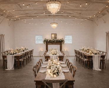 Elegant rustic wedding reception with wooden tables, white floral centerpieces, and chandeliers.