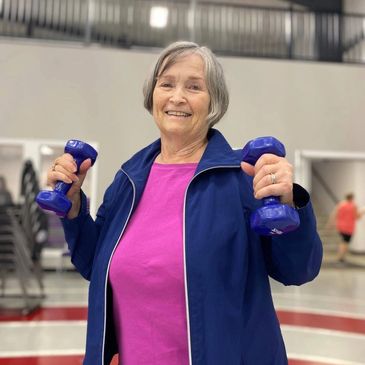 Senior member smiling while lifting blue dumbbells