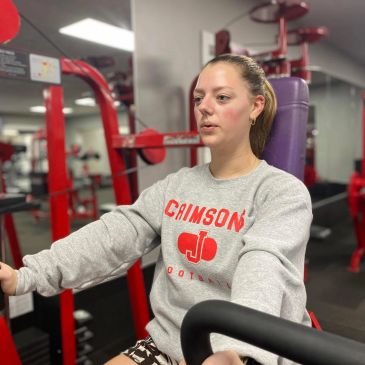Woman working out in a gym wearing a Crimson sweatshirt.