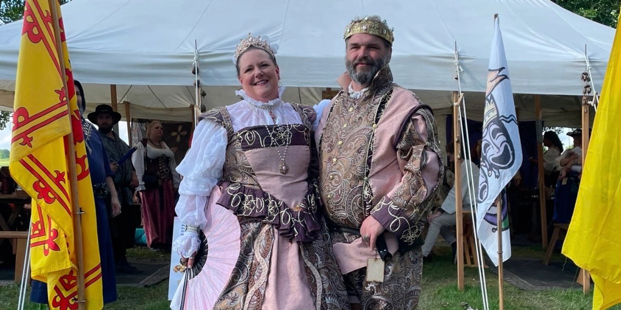 Couple dressed as a king and queen in elaborate medieval-style costumes at an outdoor event.