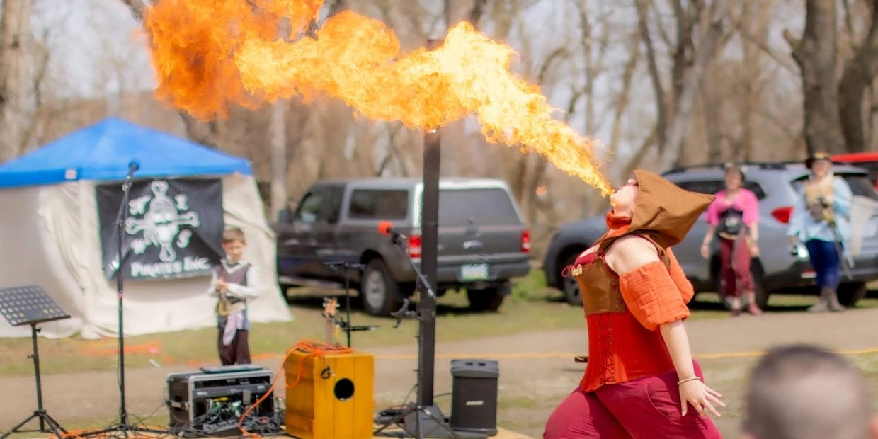 A performer breathes fire at an outdoor event surrounded by onlookers.