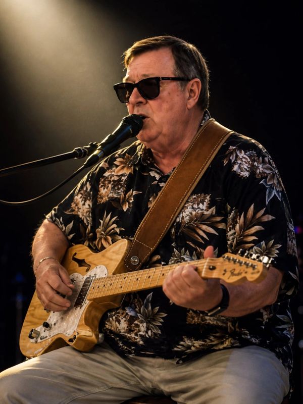 Man playing electric guitar and singing into a microphone on stage.