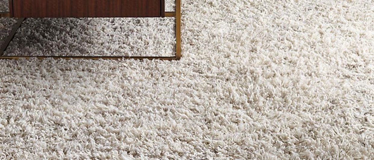 Close-up of a thick, shaggy white rug with the edge of a modern coffee table.