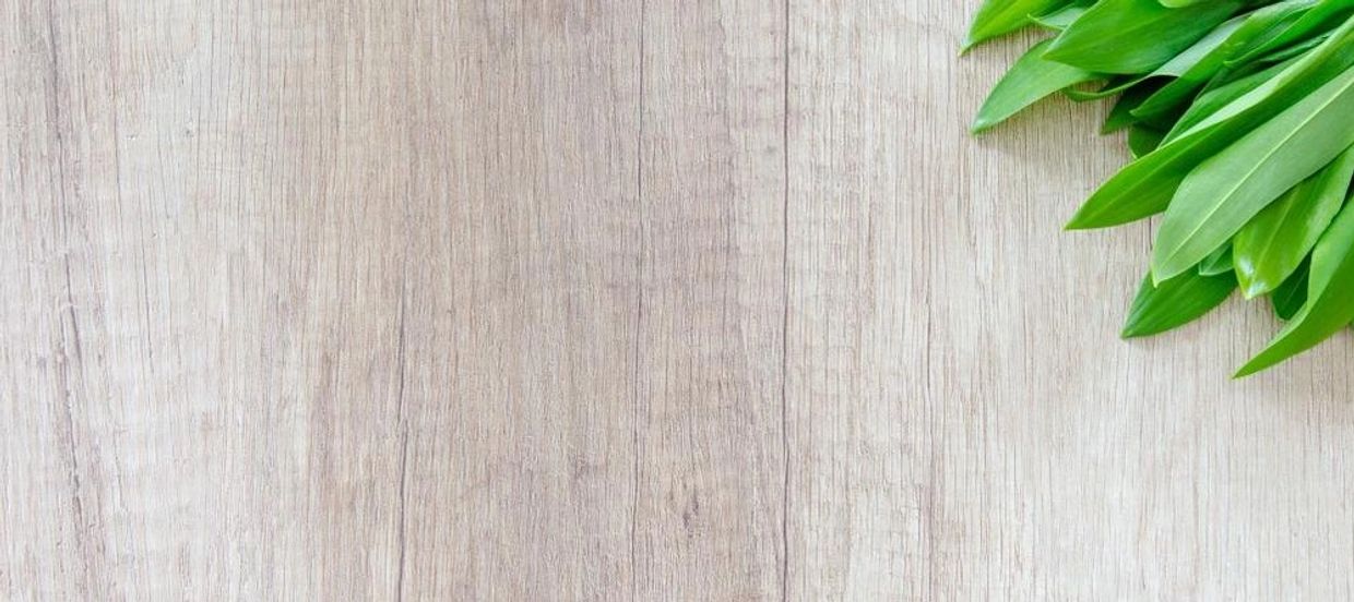 Light wooden background with a bundle of bright green leaves in the top right corner.