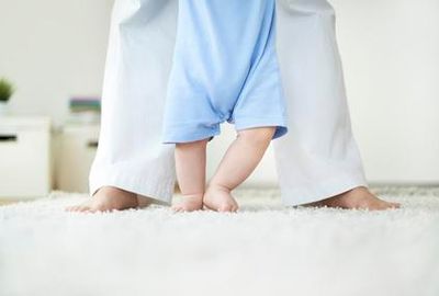Baby feet learning to walk on a white shag carpet.