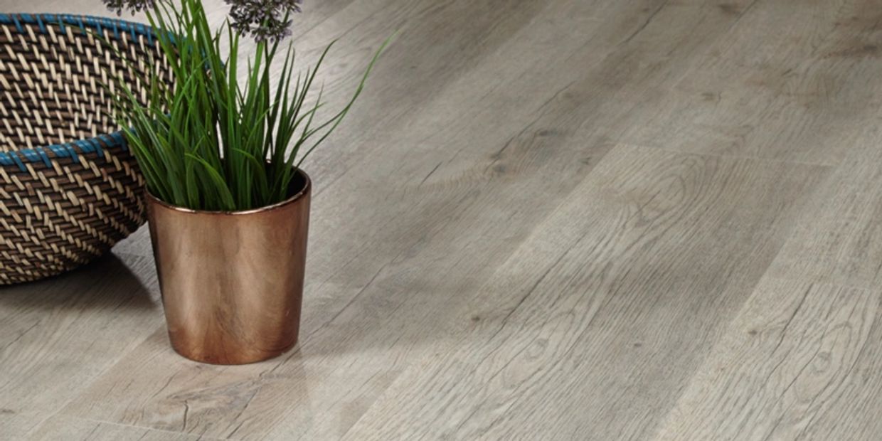 Close-up of light gray wood-look flooring with a plant in a copper pot and a basket.