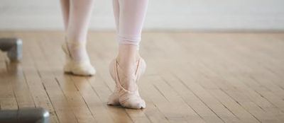 Close-up of a dancer's feet in ballet slippers on wood floor.