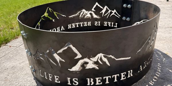 Metal fire pit with mountain cutouts and the phrase 'Life is better alone'.