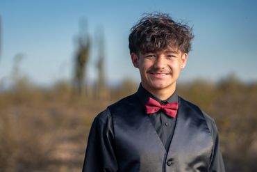 Young man in formal attire with a red bow tie smiling outdoors.