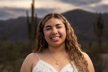 Young woman smiling outdoors with mountains and cacti in the background.