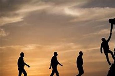 People helping each other climb a hill at sunset.