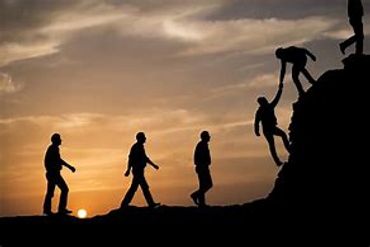 People helping each other climb a hill at sunset.