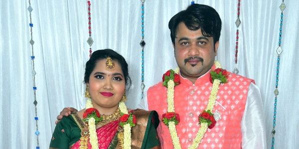 A couple dressed in traditional Indian attire with garlands poses for a photo.