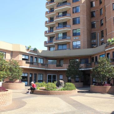 A person sitting alone in a courtyard surrounded by a large brick building.