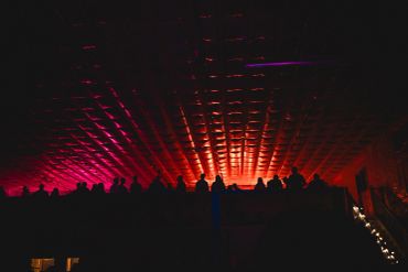 Silhouettes of people under a glowing red and purple ceiling at private music night. Lots of faces i
