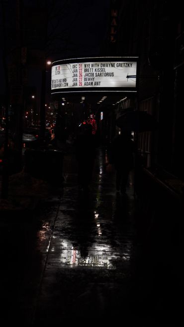 Rainy night atmospheric shot outside concert venue for performance aesthetic.