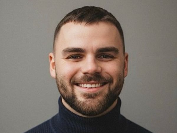 A smiling man with a beard wearing a dark turtleneck sweater.