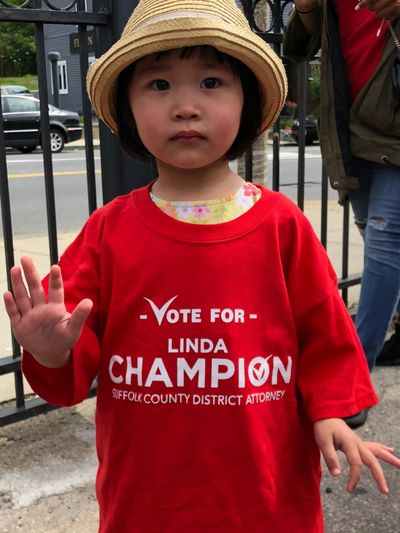 Child wearing a red campaign t-shirt and a straw hat, waving at the camera.