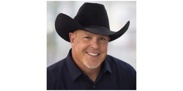 Smiling man wearing a black cowboy hat and dark shirt.