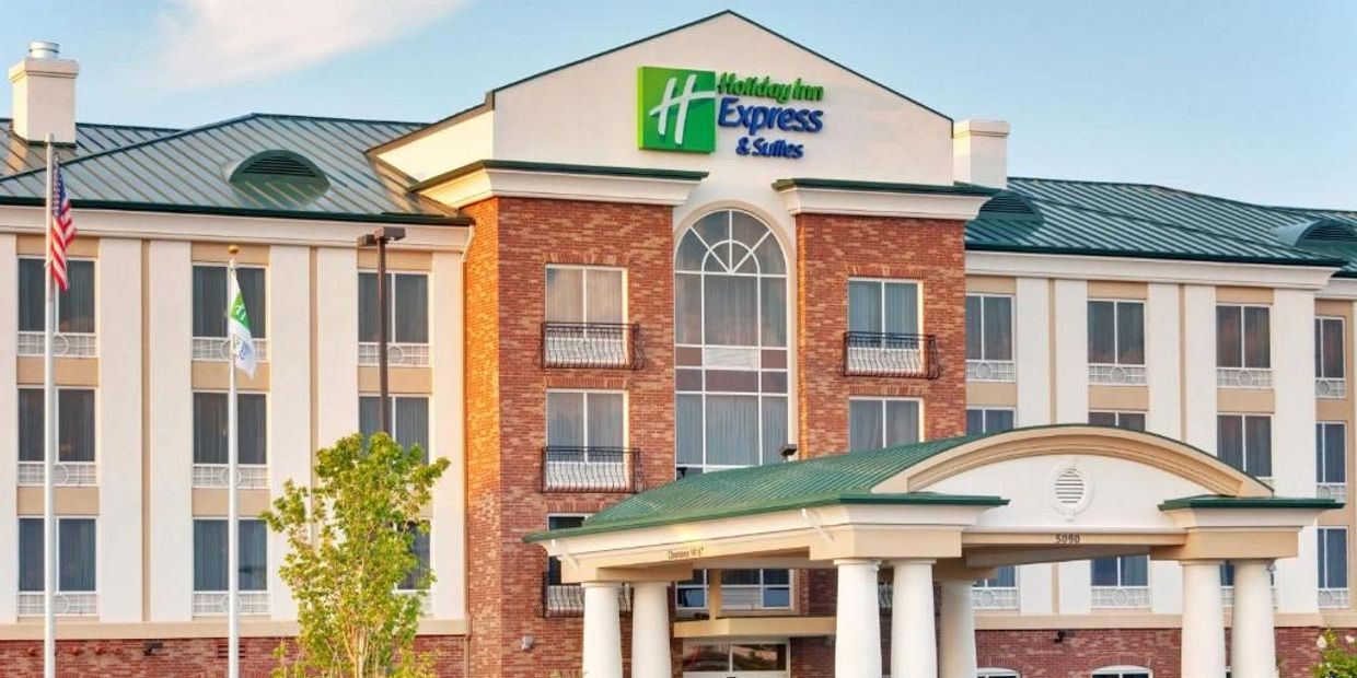 Front view of a Holiday Inn Express & Suites hotel building with flags and a clear sky.