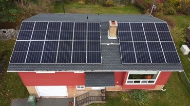 Solar panels installed on the roof of a red house.