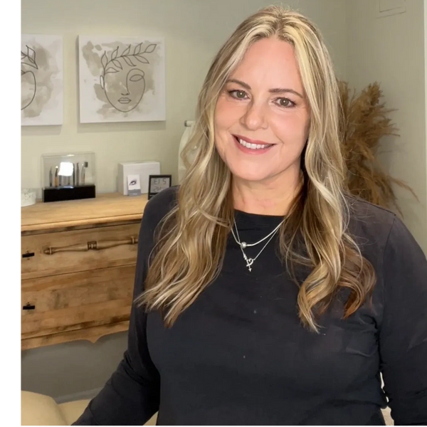 Smiling woman with blonde hair in a cozy room with wooden furniture and minimalist art.