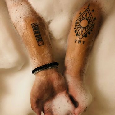 Two tattooed forearms submerged in a foam-filled bath, one with a bracelet.