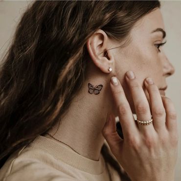 Close-up of a woman with a small butterfly tattoo on her neck.
