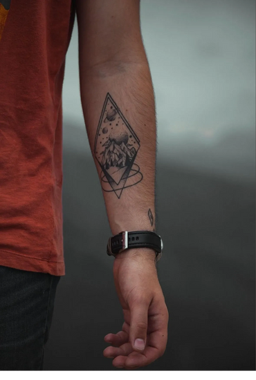 Forearm tattoo of mountains and planets within geometric shapes.