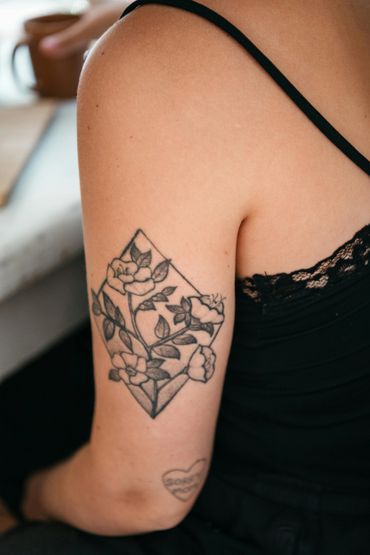 Floral tattoo with leaves inside a geometric diamond shape on upper arm.